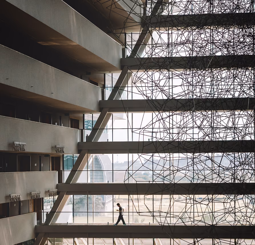 Person walking in a modern building with large glass windows and geometric wire installation.