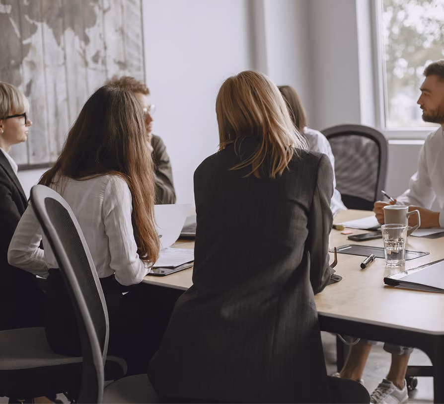 Five businesspeople seated around a conference table having a meeting in an office with a window.
