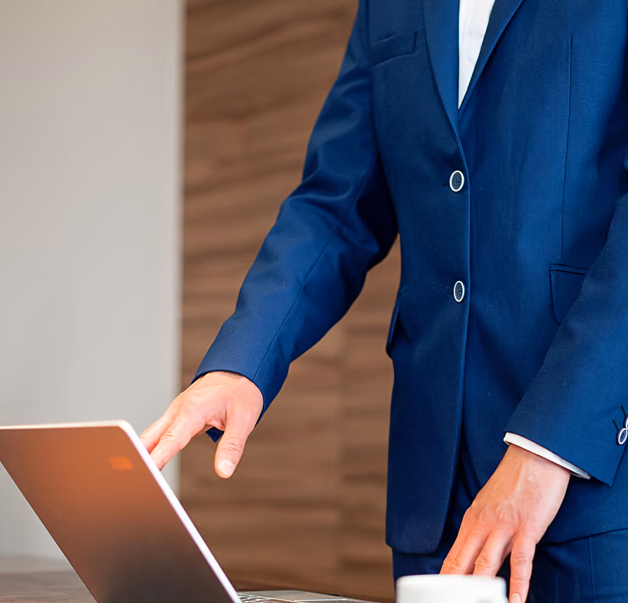 Person in navy blue suit interacting with a laptop on a table in an office.