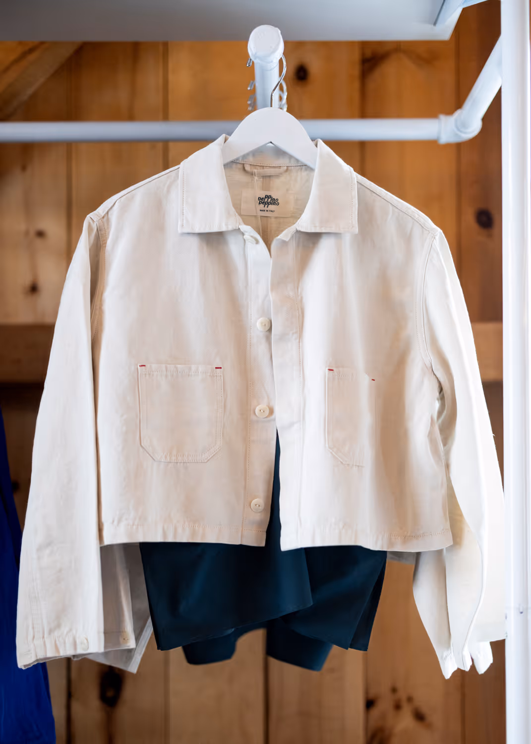 Cropped beige jacket with front pockets hanging on a white hanger against a wooden background.