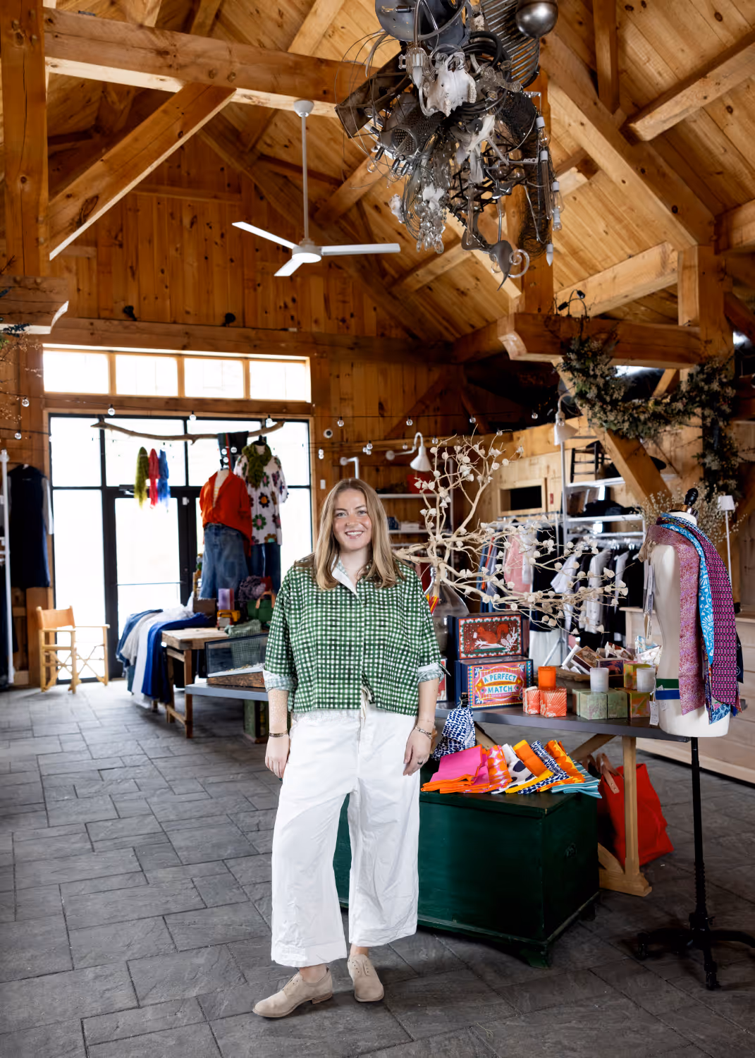 Smiling woman stands in a boutique with wooden walls, colorful clothes, and decorative items.