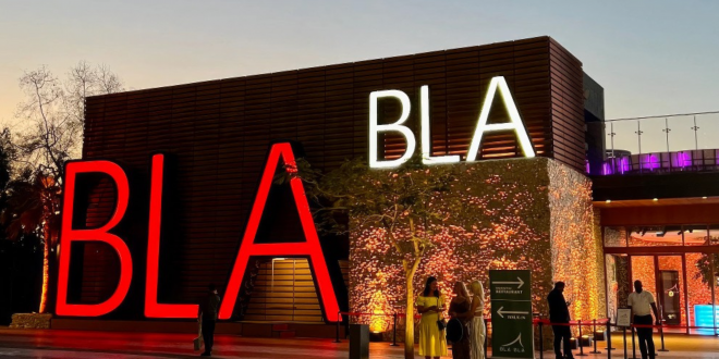 Building exterior at dusk with large red and white BLA letters and people standing nearby.