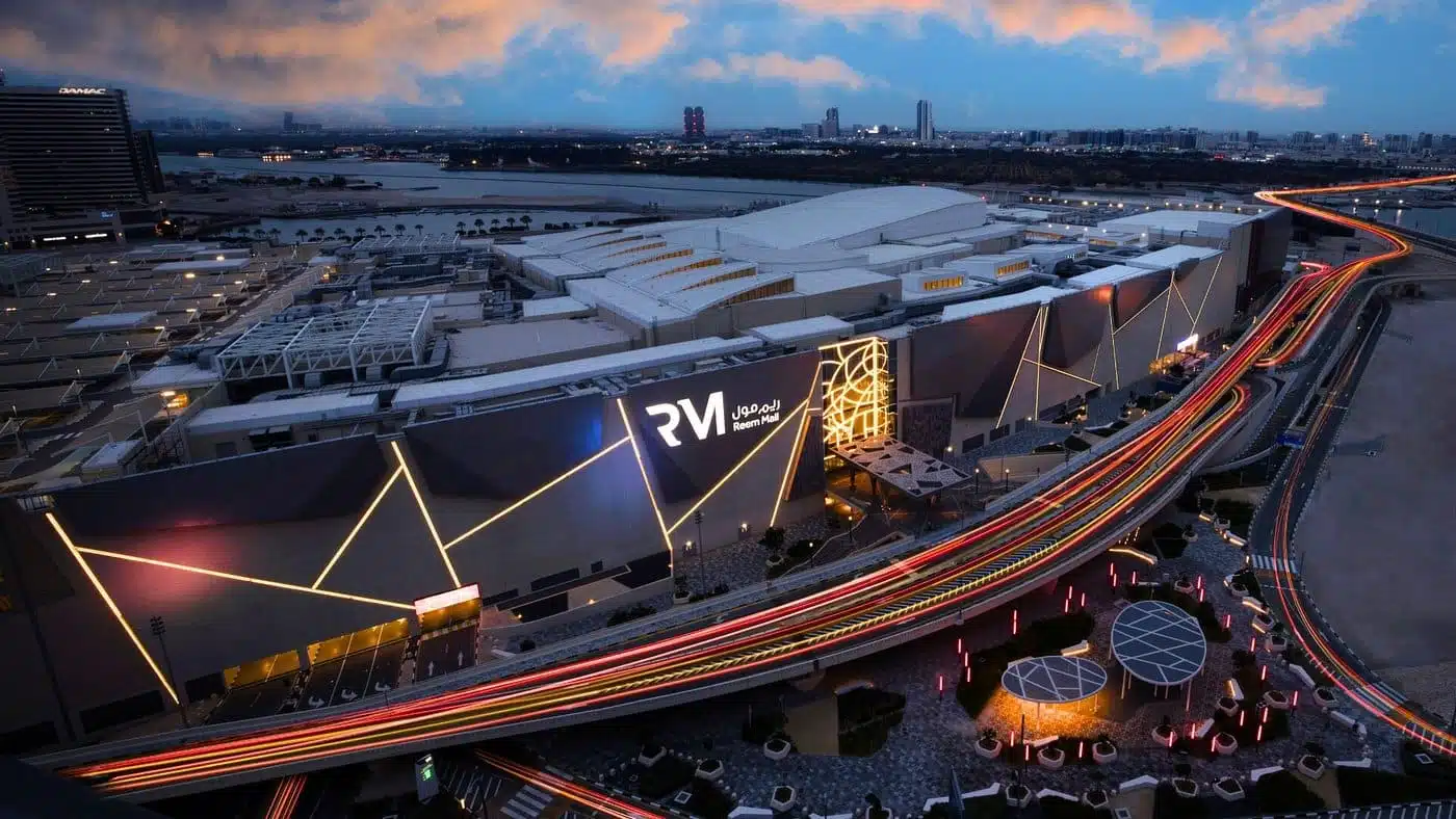 Night aerial view of Reem Mall with illuminated geometric facade and light trails on elevated roads.