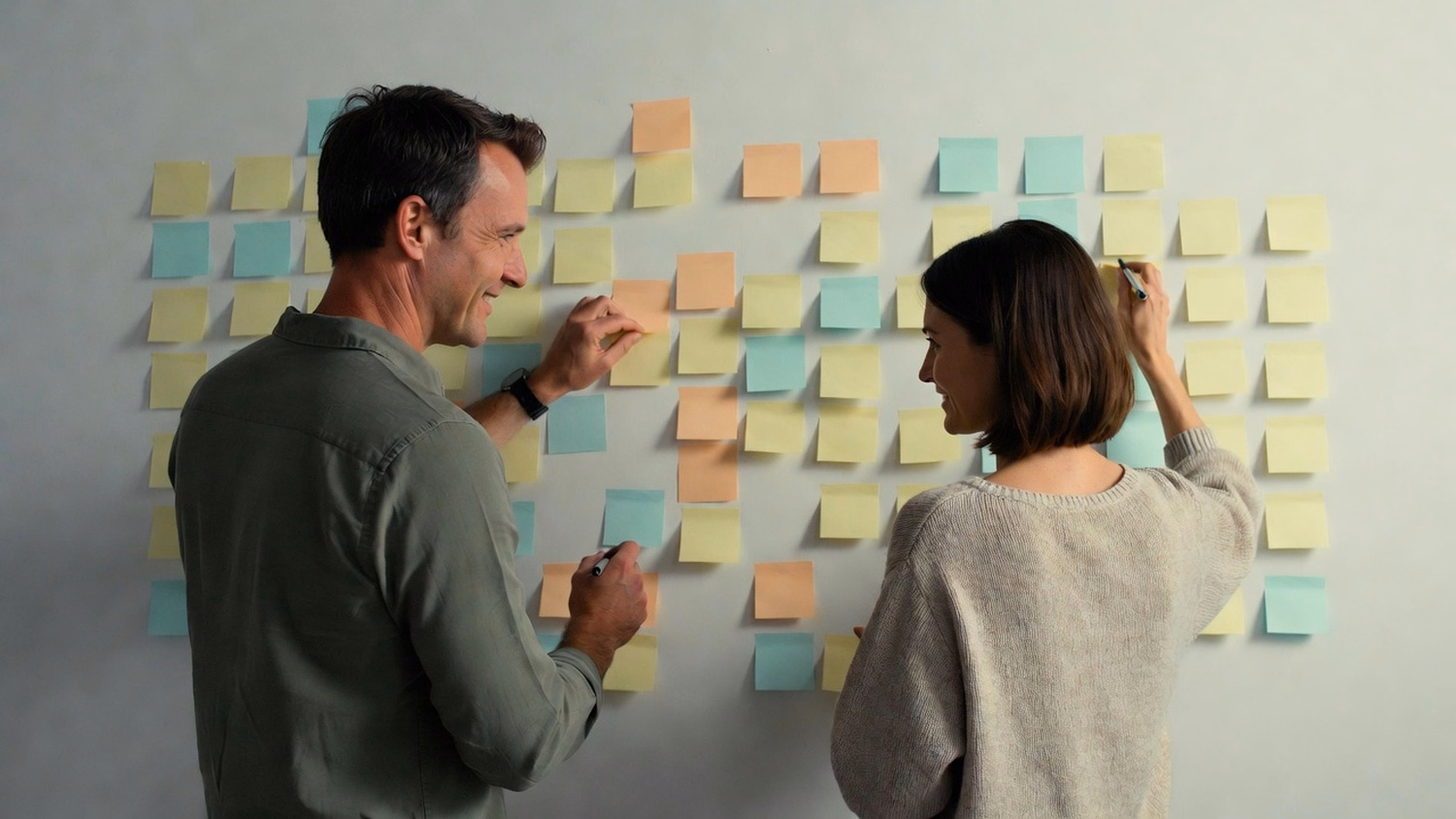 STICKY NOTE WALL Two people, a man and a woman, stand facing a wall plastered