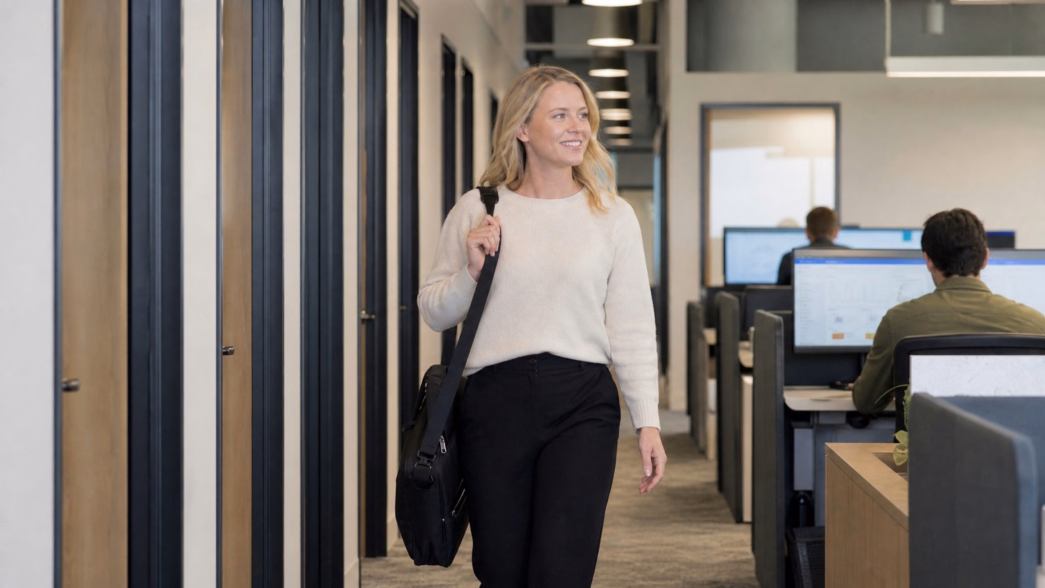 Woman walks down office corridor with laptop bag