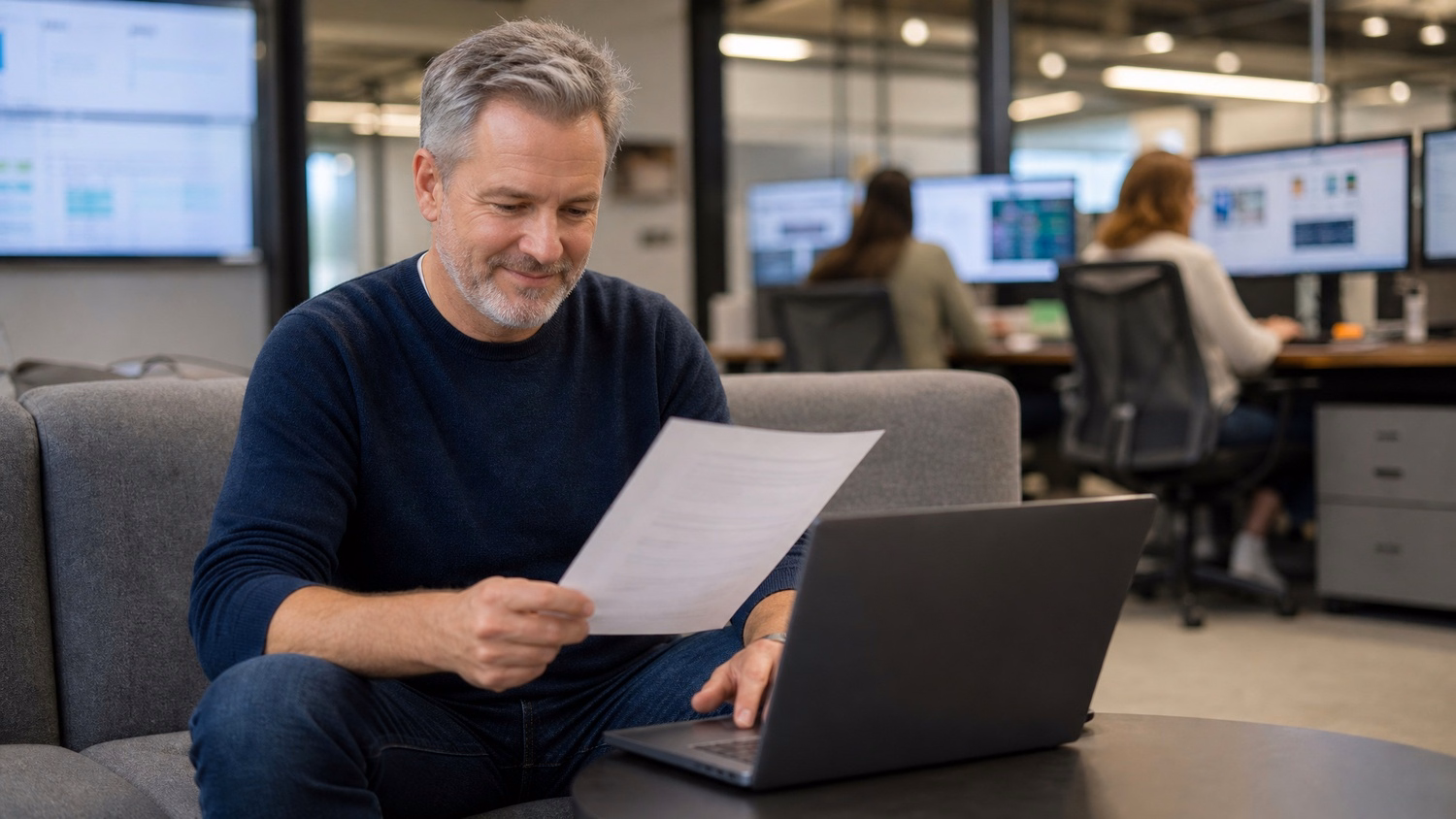 Man reviews compliance document on laptop in lounge area 64 chars