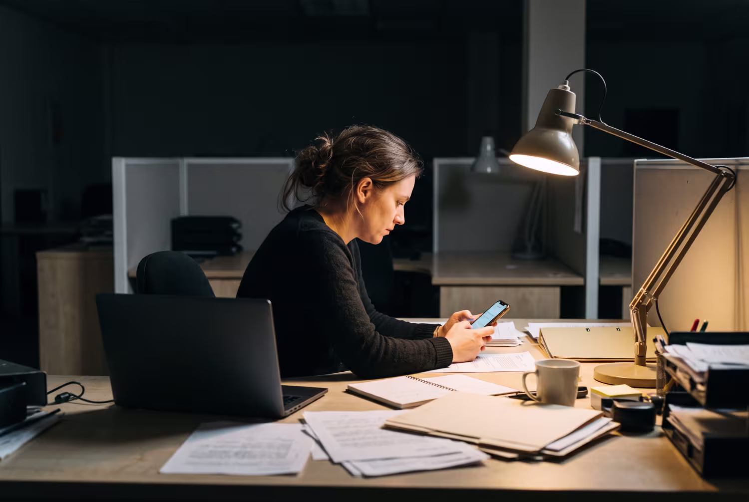 Staff member using smartphone at dimly lit office desk