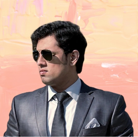 Man wearing a gray suit, white shirt, and black tie with a white pocket square, wearing dark sunglasses, looking to the left.