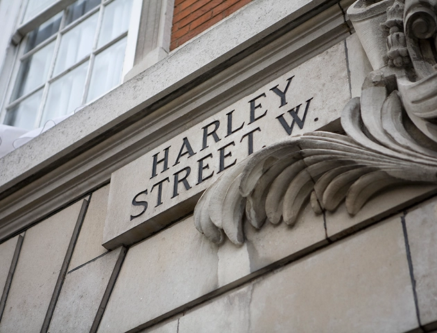 Stone street sign reading 'HARLEY STREET W.' mounted on a building with decorative stone carvings and windows.