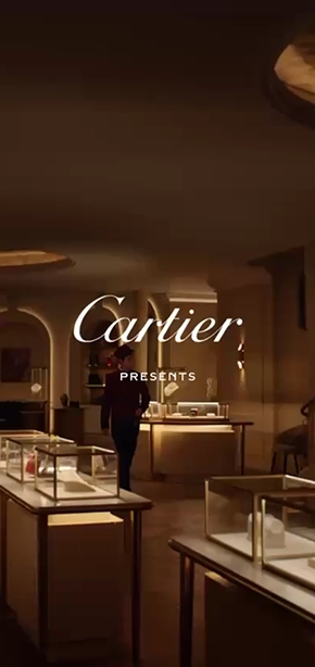 Luxurious Cartier jewelry store interior with glass display cases showing various jewelry pieces, warm lighting, and a person standing near a display in the background.