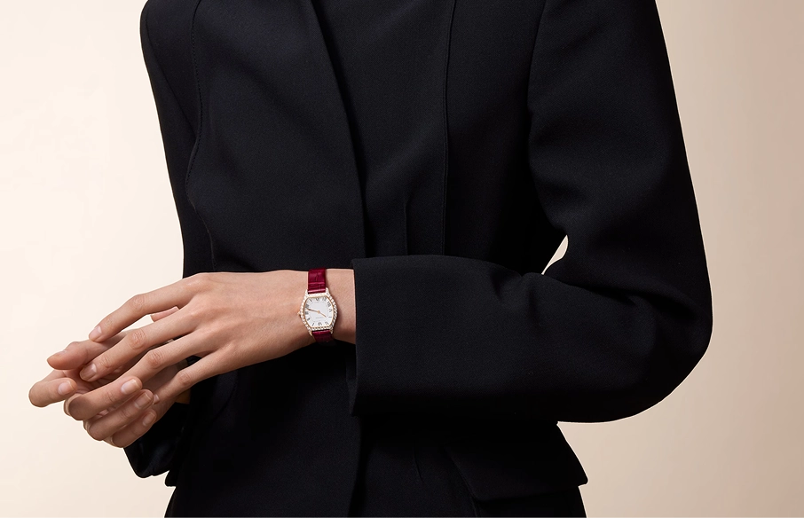 Close-up of a person wearing a black blazer, showing a wristwatch with a silver face and a red leather strap on the left wrist.