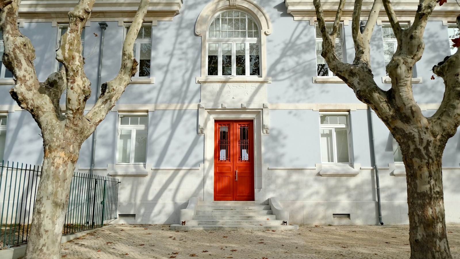 Façade d'un établissement scolaire ancien, porte rouge et platanes : avocat des OGEC, enseignement catholique