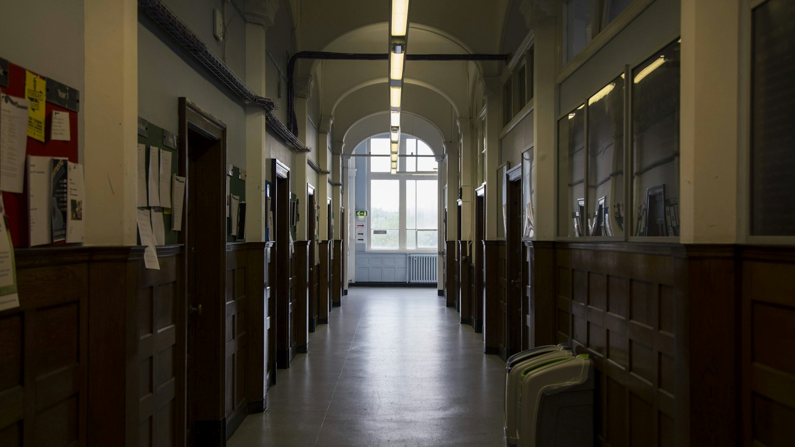 Couloir ancien d'un établissement d'enseignement, boiseries et panneaux d'affichage : les personnels de l'OGEC