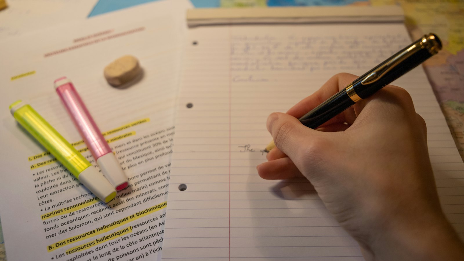 Main écrivant au stylo plume sur une copie, documents surlignés à côté : les contrats de l'établissement OGEC
