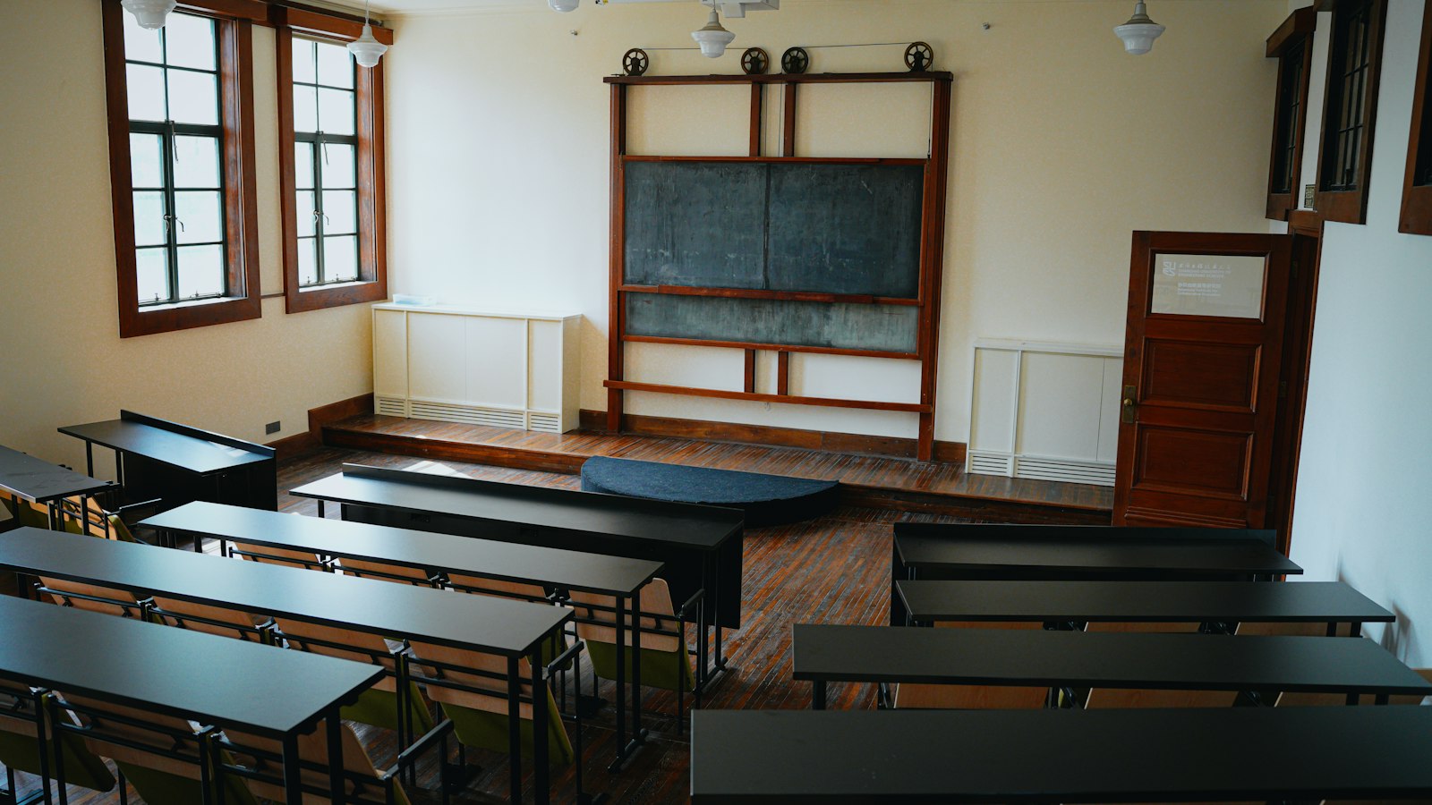 Salle de classe ancienne, tableau noir, estrade et rangées de tables : identification de l'employeur en OGEC