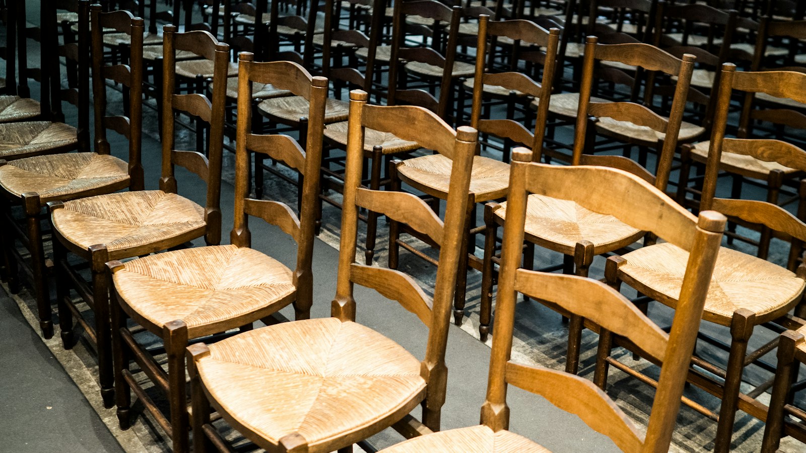 Rangées de chaises paillées en bois dans une salle d'assemblée : statuts types et instances de l'OGEC