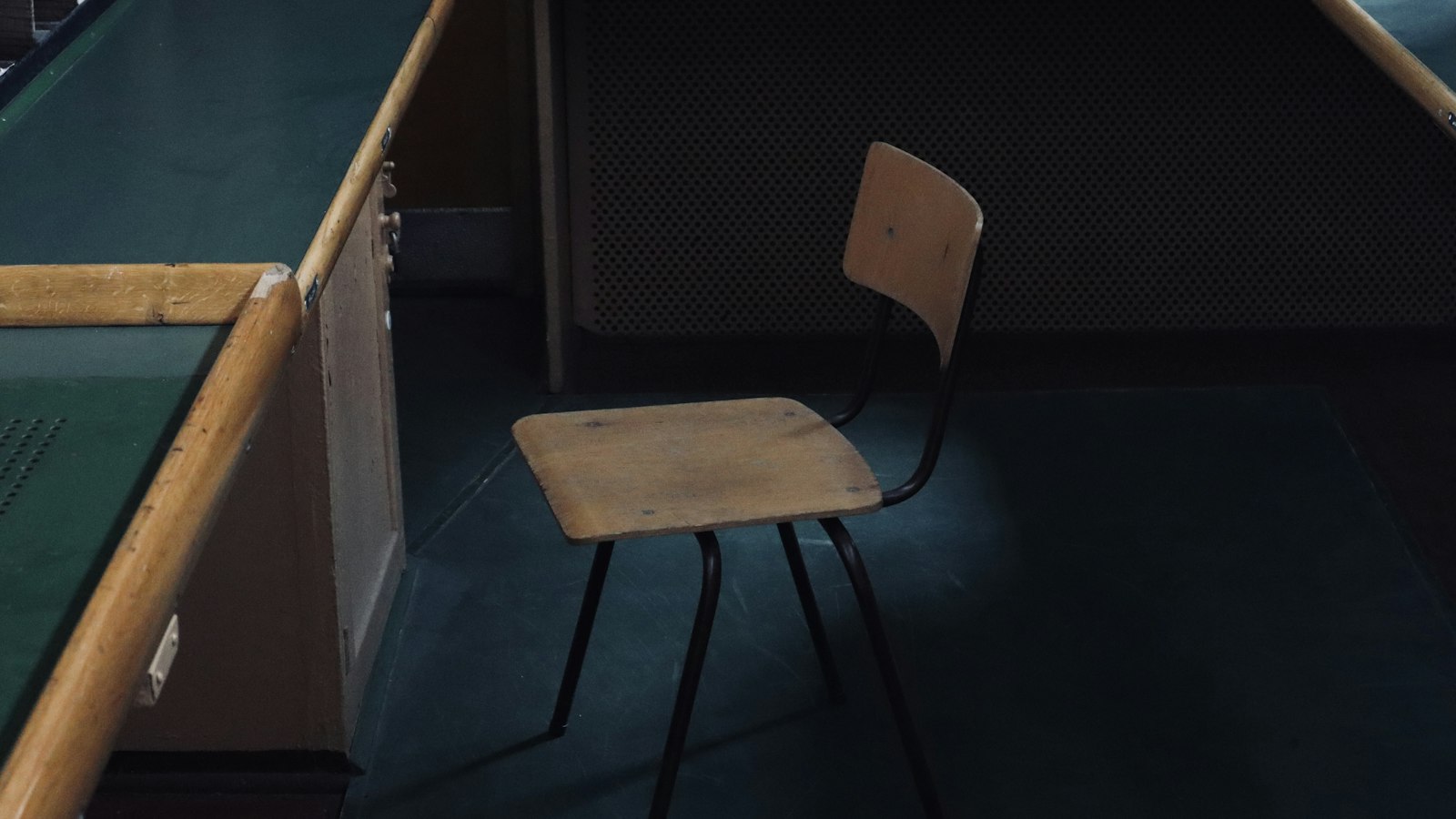 Chaise d'école vide dans une pièce sombre, entre des bureaux à plateau vert : retrait de mission et rupture du contrat