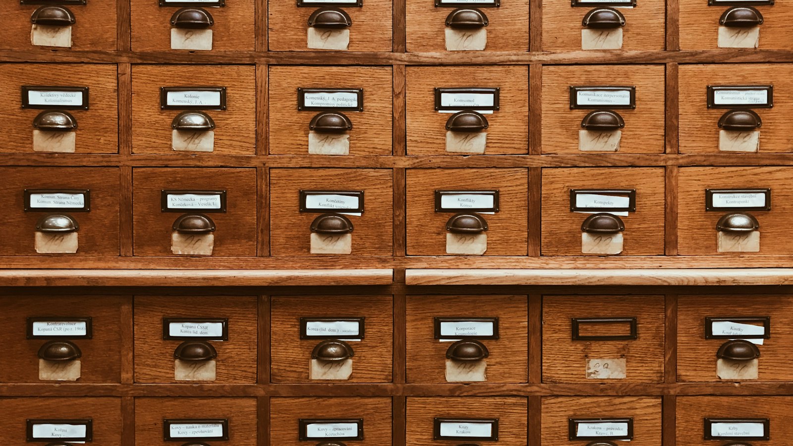 Tiroirs de fichier en bois étiquetés, alignés en rangées : classification des postes des salariés d'OGEC