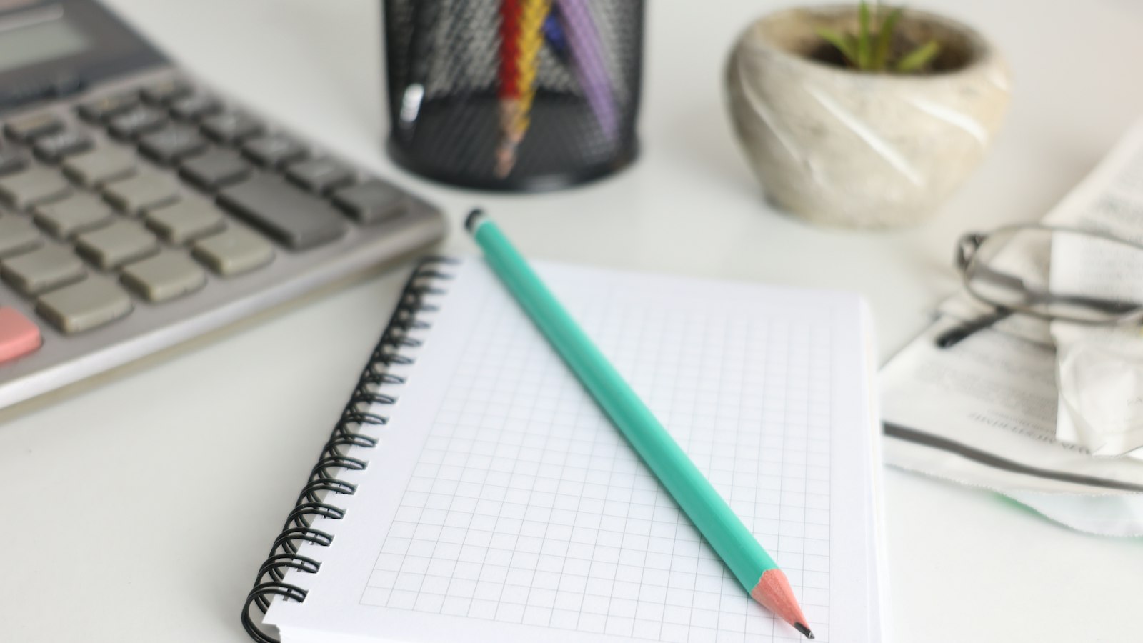 Calculatrice, cahier à petits carreaux et crayon sur un bureau clair : salaires minima des salariés des OGEC
