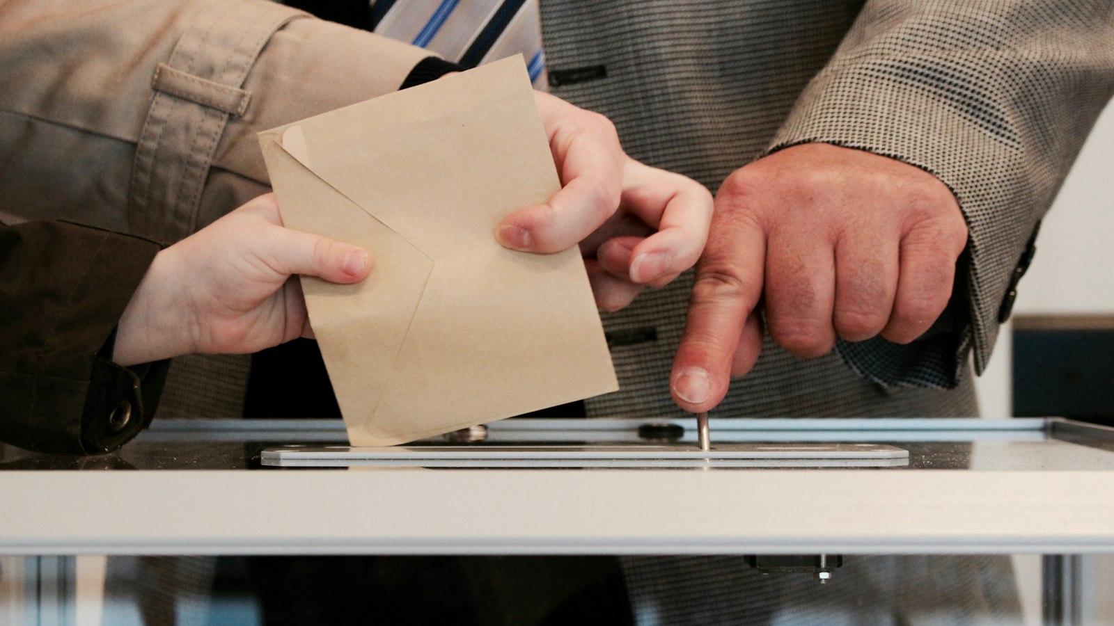 Mains glissant une enveloppe kraft dans une urne transparente : élections professionnelles du CSE en OGEC