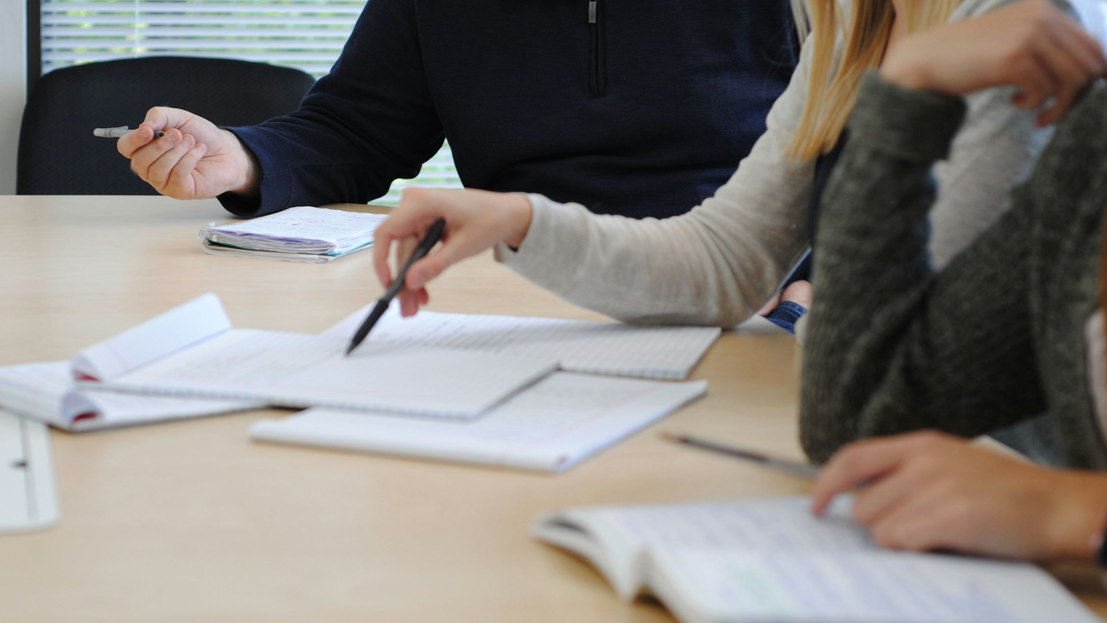 Mains de 3 personnes au travail autour d'une table, cahiers ouverts : chef d'établissement et enseignants agents publics