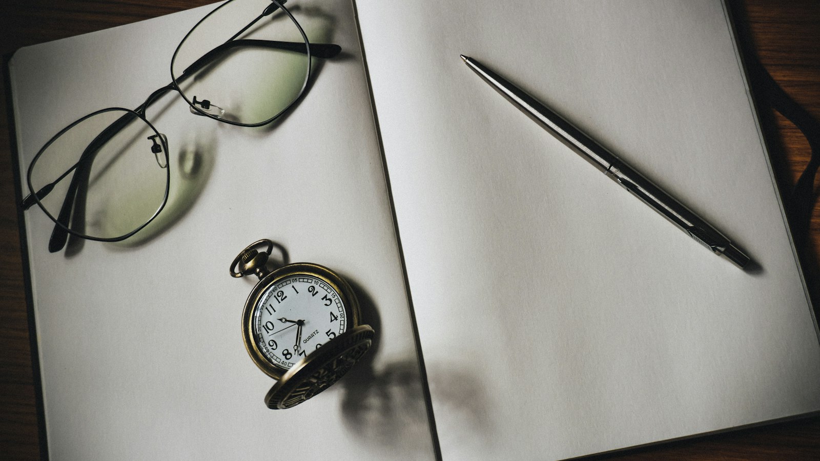 Montre de gousset, lunettes et stylo sur un carnet ouvert : rémunération et temps de travail du chef d'établissement