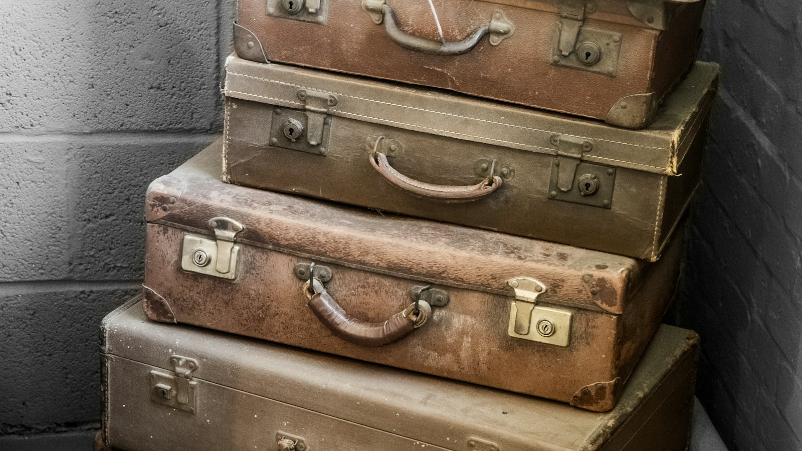 Pile de valises anciennes contre un mur gris : les frais professionnels des salariés de l'OGEC