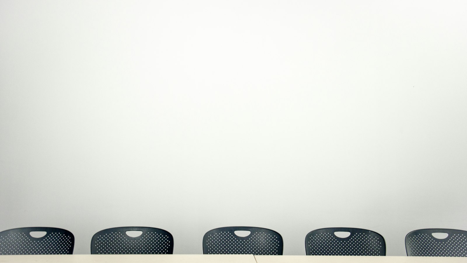 Rangée de chaises noires contre un mur blanc : le recrutement d'un salarié par l'OGEC
