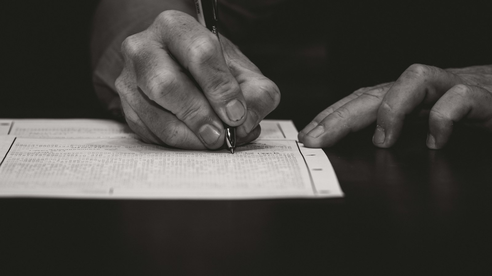 Main remplissant un document au stylo, en noir et blanc : les formalités d'embauche dans les hôtels, cafés, restaurants