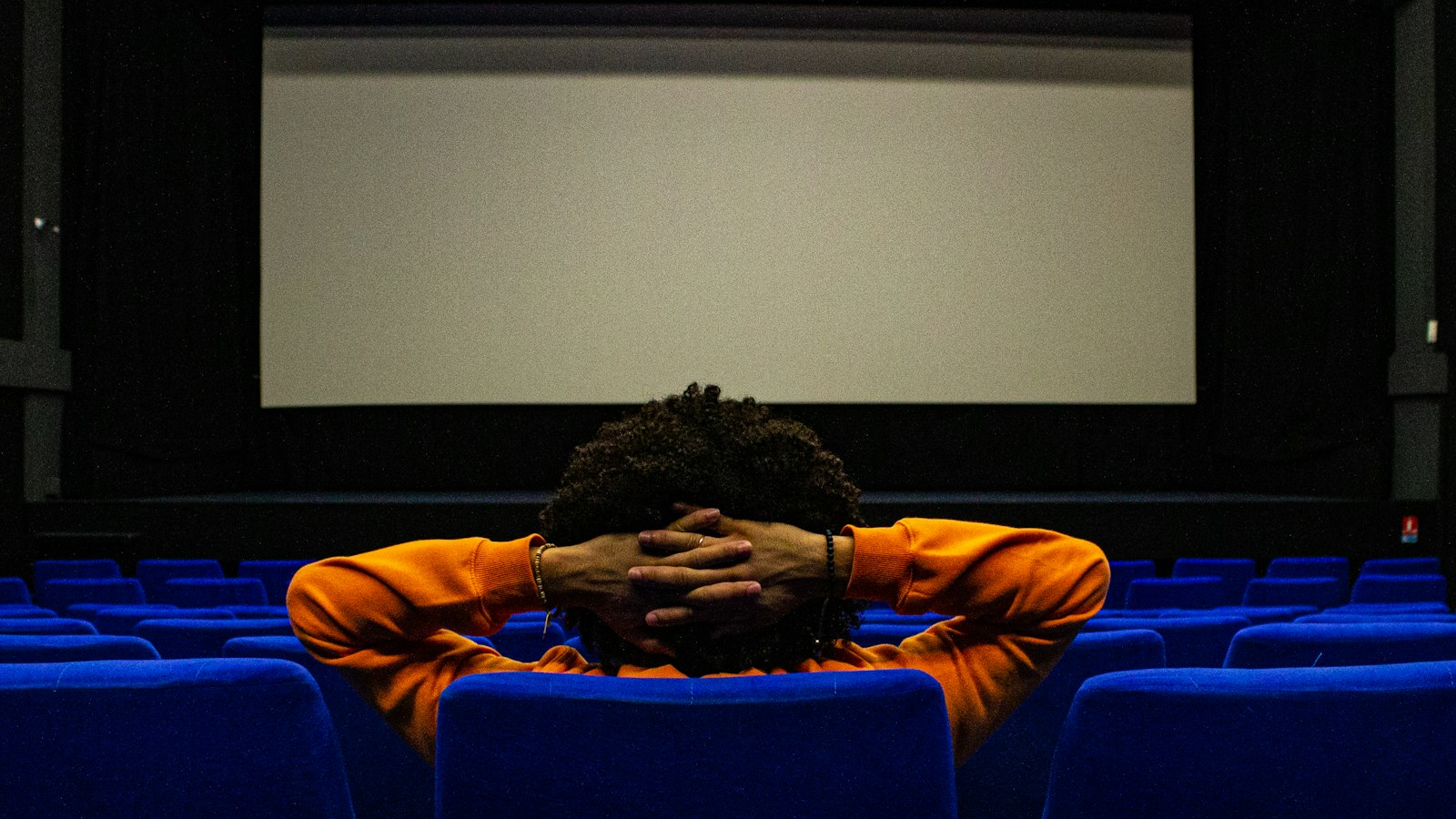 Personne seule assise de dos face à un écran de cinéma : questions fréquentes des exploitants de cinéma