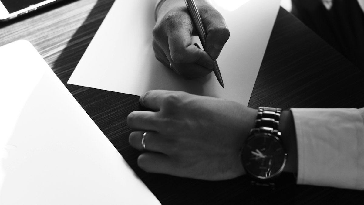 Main signant un document sur un bureau, en noir et blanc : l'embauche et le contrat de travail dans une entreprise de propreté