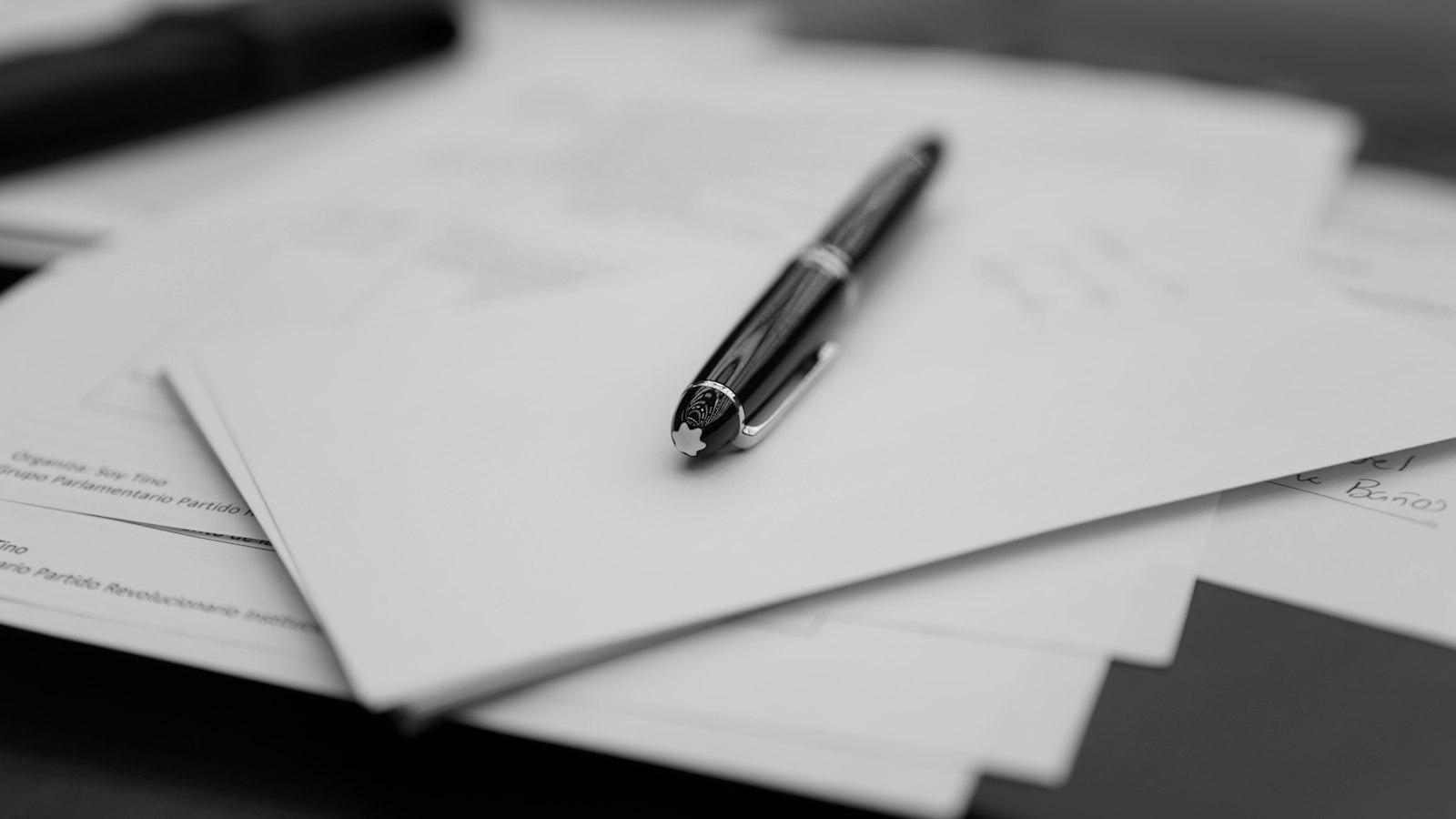 Stylo posé sur une pile de documents, en noir et blanc : le règlement intérieur et les sanctions dans une entreprise de propreté