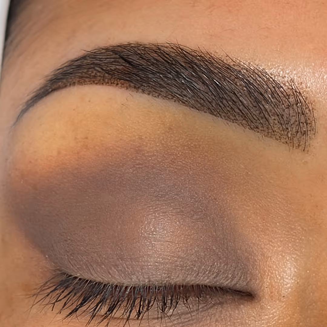Closed eye with well-defined dark eyebrow and blended purple eyeshadow on eyelid.