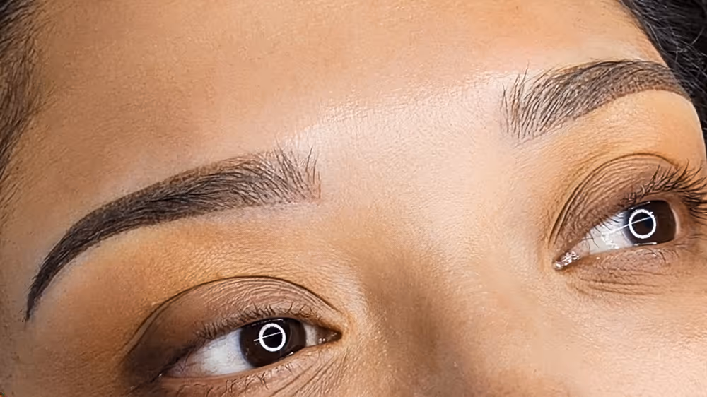 Close-up of well-groomed eyebrows and eyes with brown eyeshadow on light brown skin.
