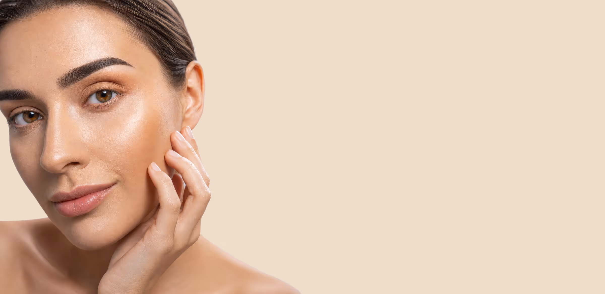 Close-up of a woman with smooth skin gently touching her face against a light beige background.