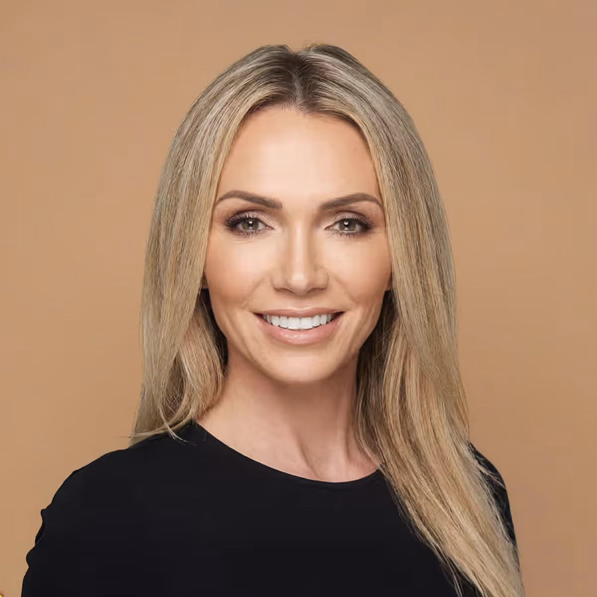 Lilli Escobar smiling with long blonde hair wearing a black top against a plain beige background.