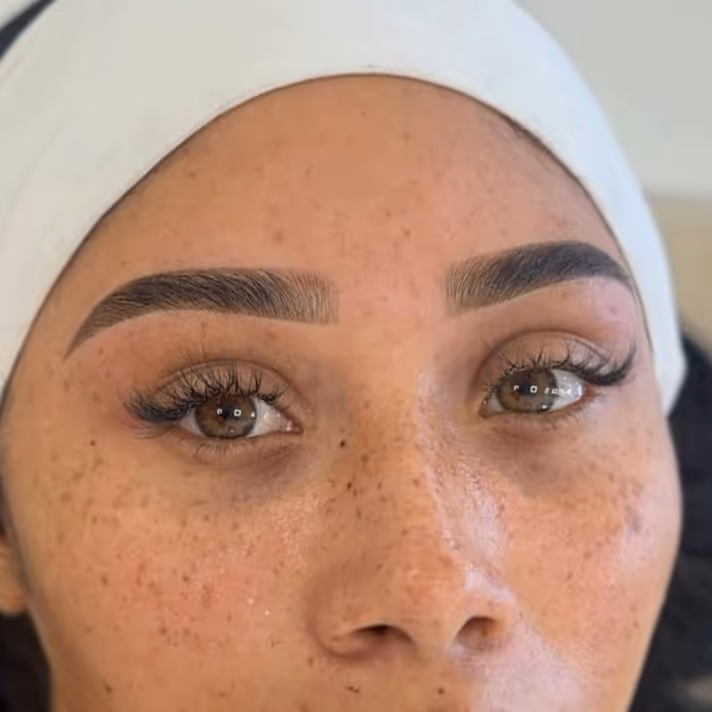 Close-up of a woman's freckles and perfectly shaped, tinted eyebrows with long eyelashes.