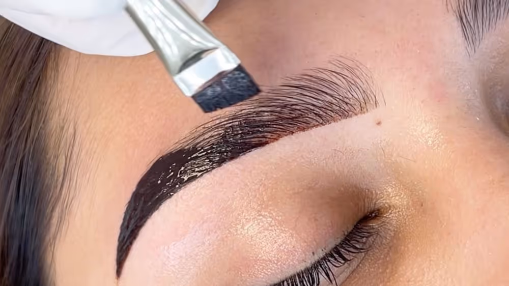 Close-up of dark tint being applied to a woman's eyebrow with a brush.