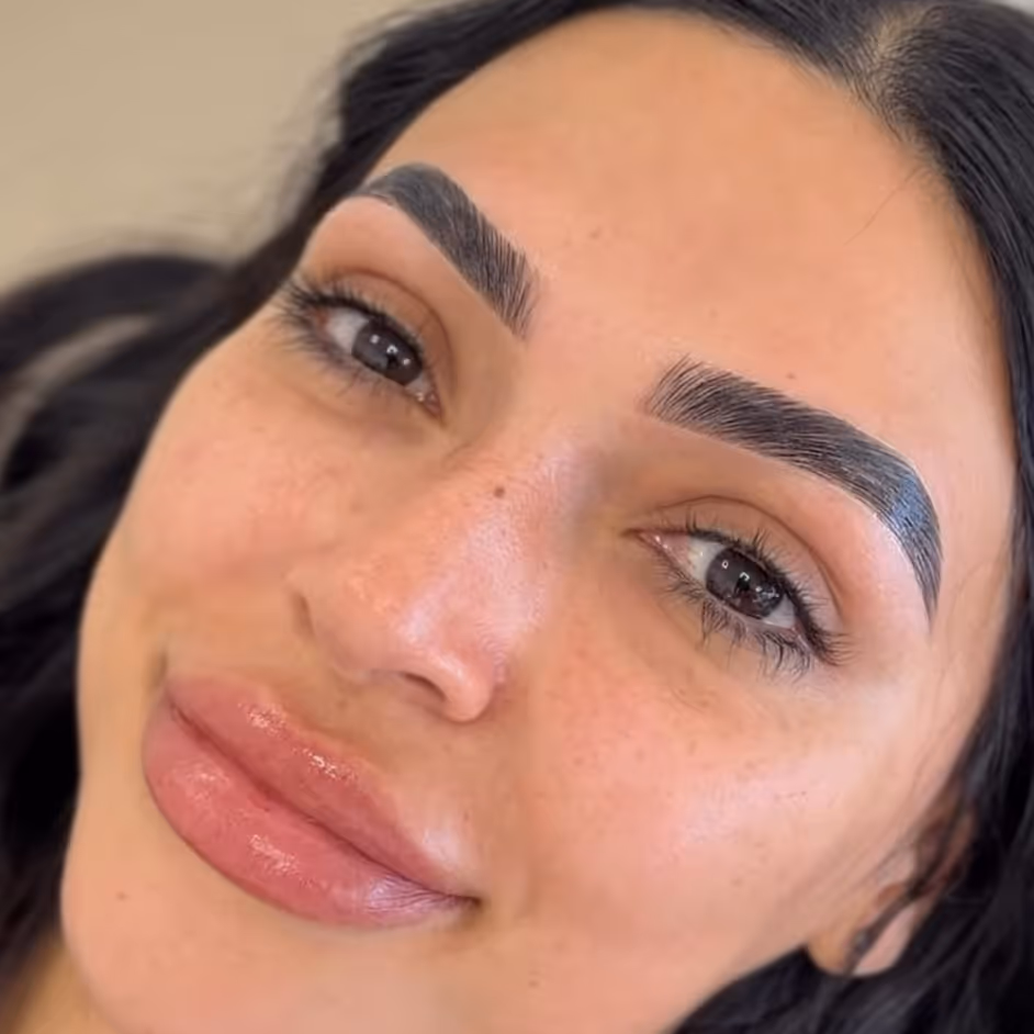 Close-up of a woman with perfectly shaped, tinted, and laminated eyebrows and glossy lips.