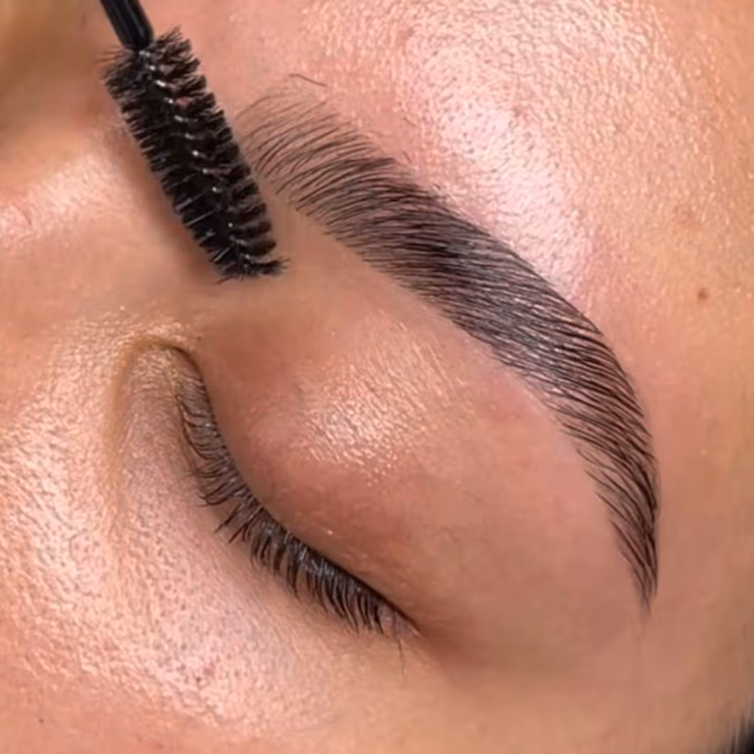Close-up of an eye with groomed eyebrow being brushed with a spoolie brush.