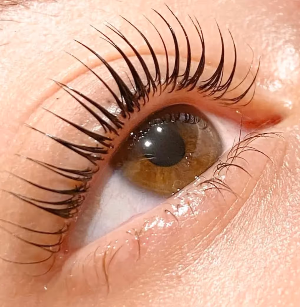 Close-up of a brown eye with long, curled eyelashes against smooth skin.