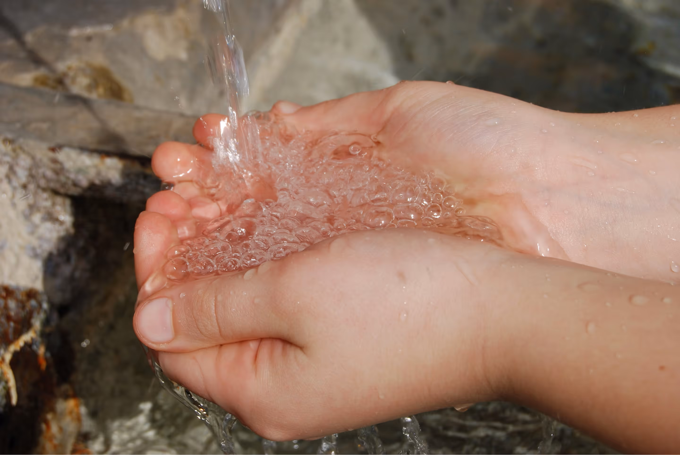 Two hands cupped together holding clear, bubbly water flowing from above.