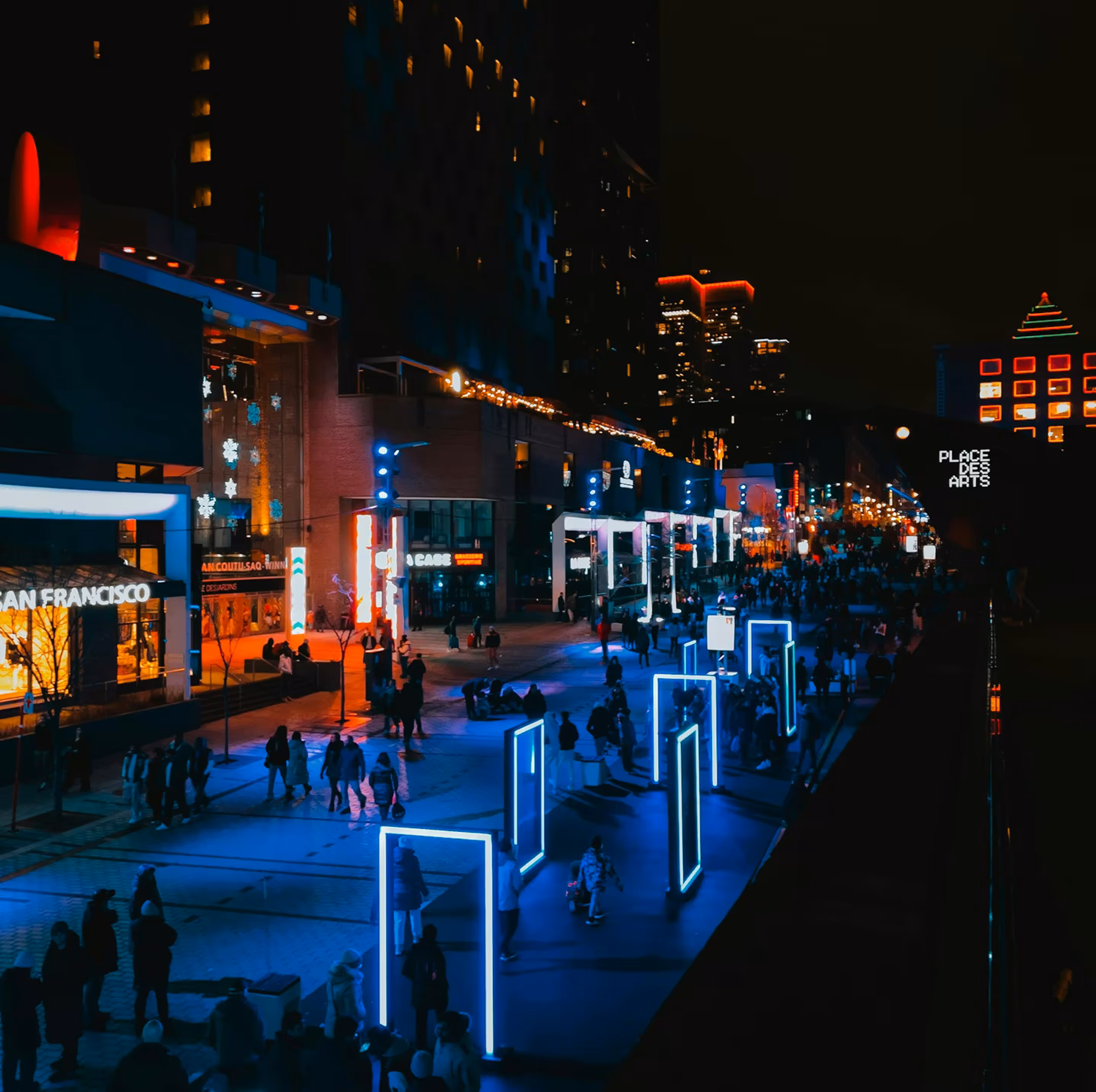 Crowded city street at night with illuminated blue rectangular light frames and tall buildings with lights.
