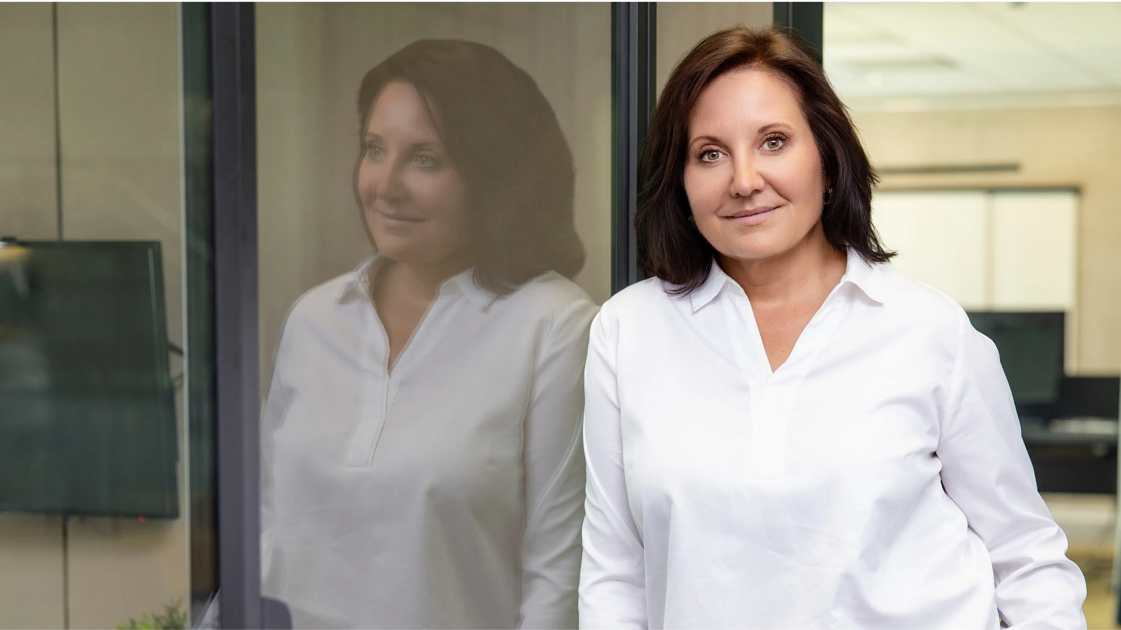 Marion Mossmann Schwarz, Expertin für Kundenakademien und messbaren Kundenerfolg, im weißen Hemd vor einer Glasfläche.