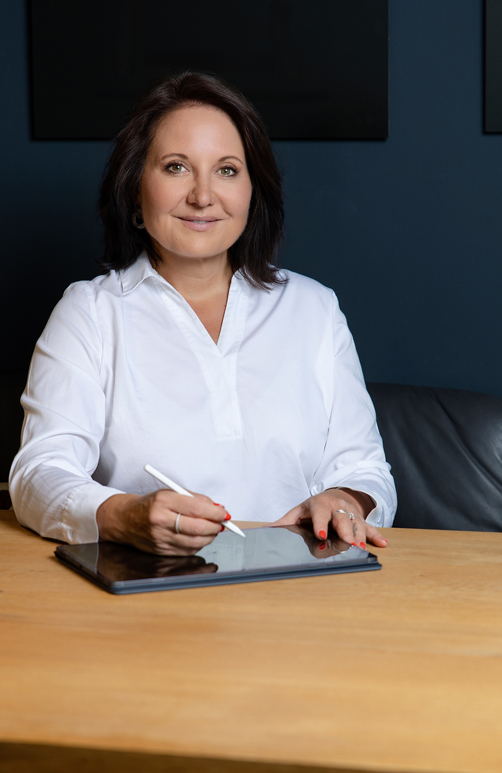 Marion Mossmann Schwarz sitzt am Tisch und schreibt mit einem Stift auf einem Tablet.