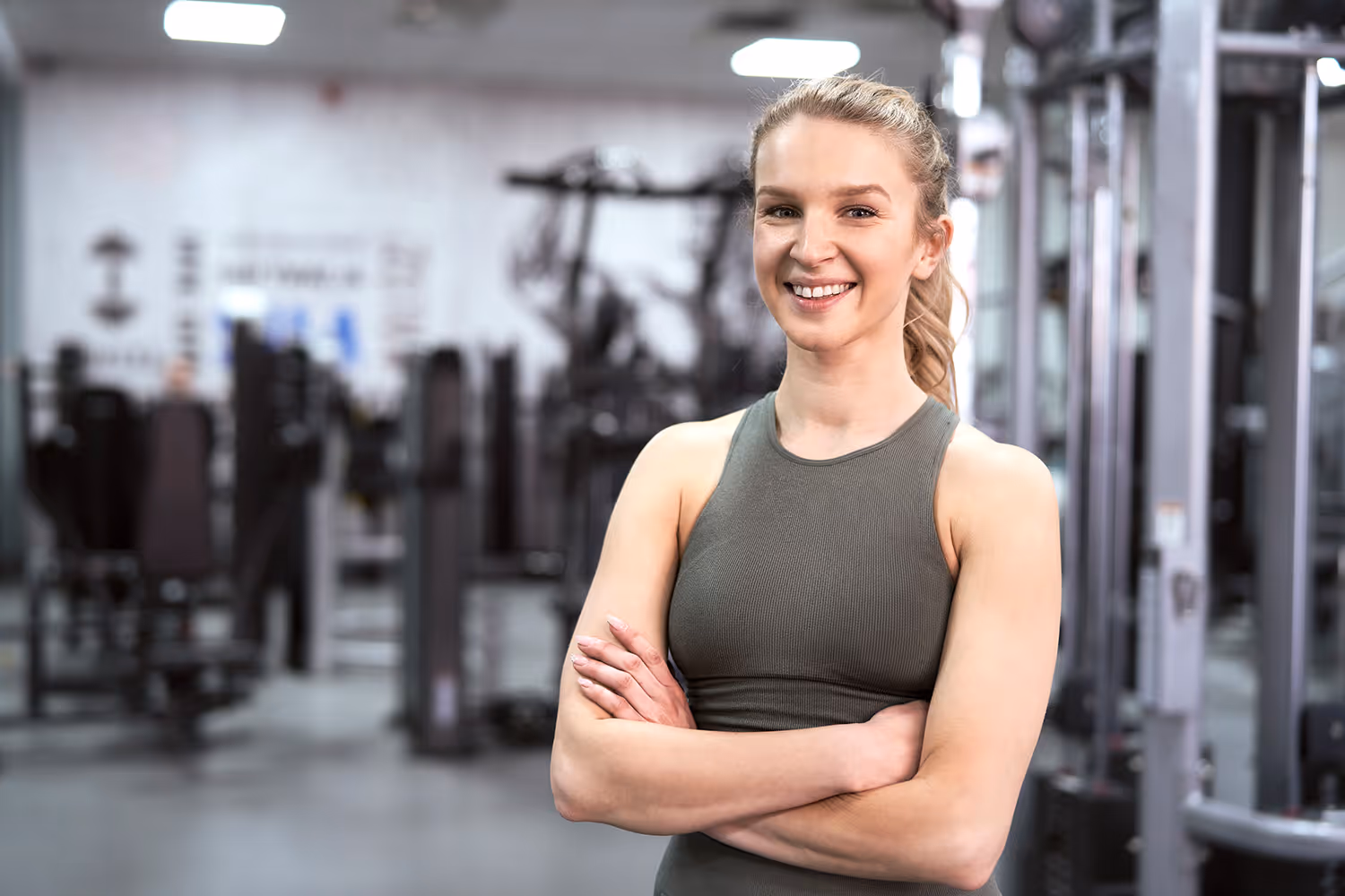Lächelnde Frau in Sportkleidung mit verschränkten Armen im Fitnessstudio.
