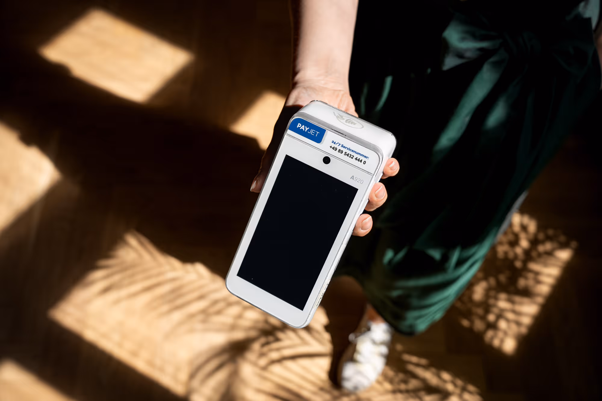 Hand präsentiert mobiles Kartenterminal für Kartenzahlung im sonnendurchfluteten Geschäft