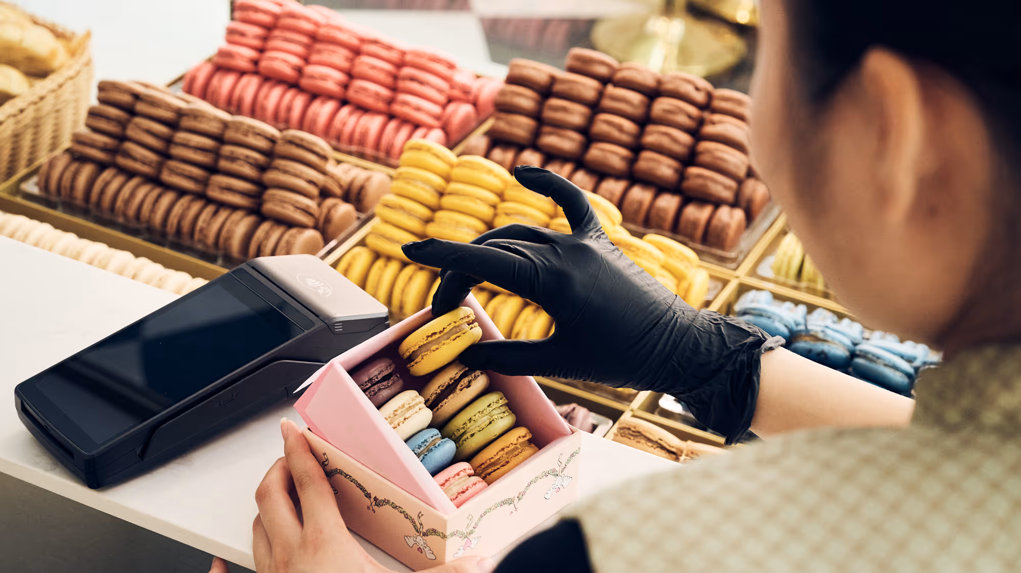 Mitarbeiterin füllt Macarons in eine Schachtel, Kartenterminal liegt auf dem Tresen
