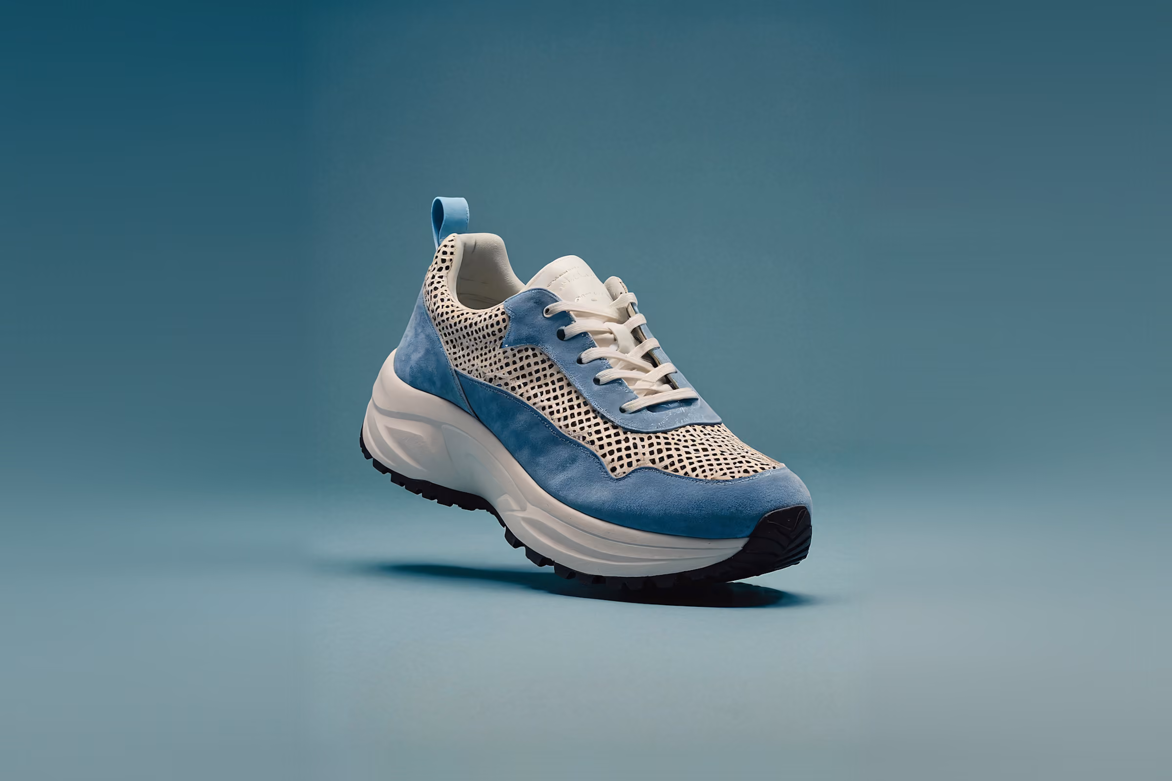 Blau-weißer Sneaker mit schwarzen Akzenten vor einfarbigem blaugrünem Hintergrund.