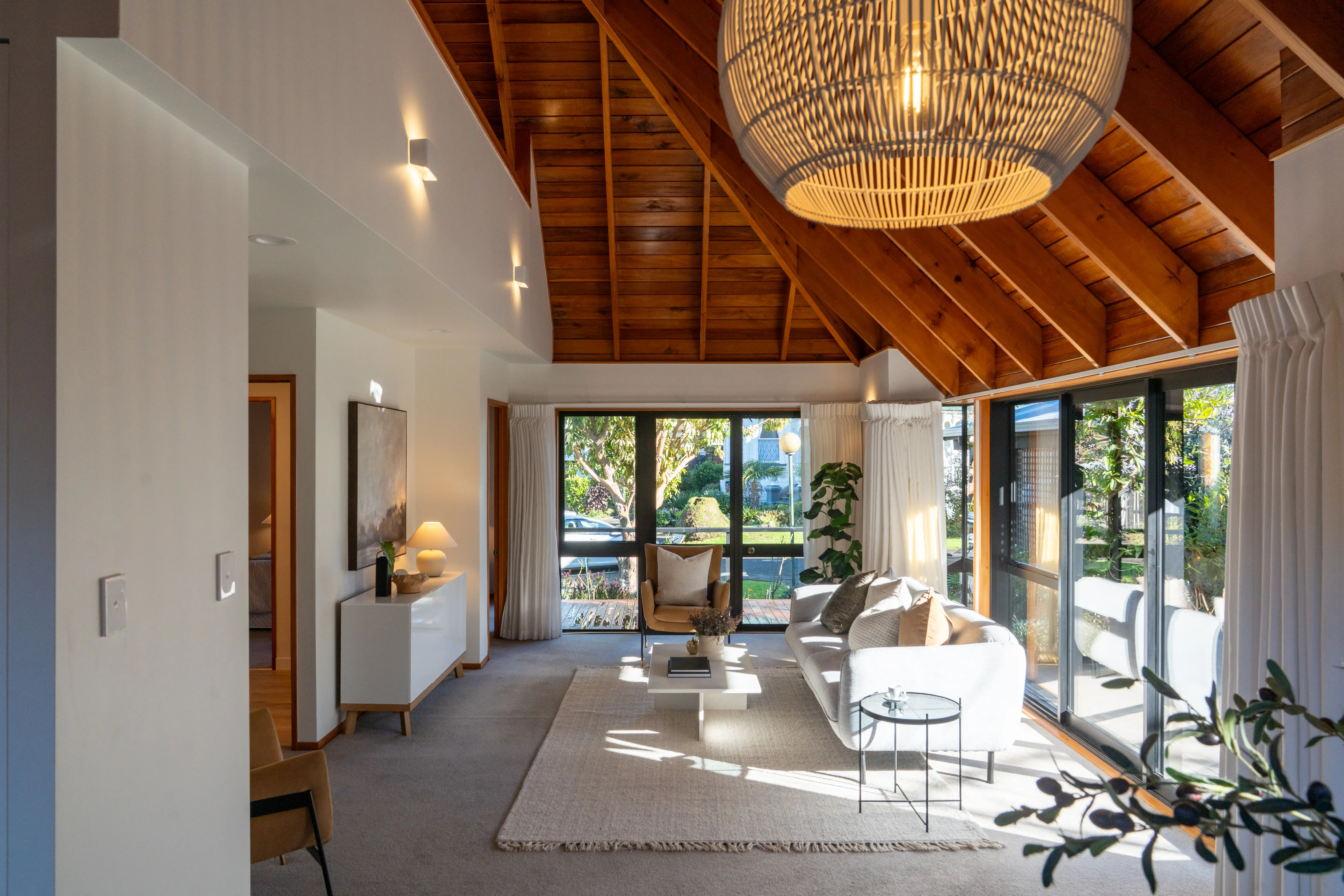 Open-plan living and dining in a villa, with a high timber ceiling and full-height glass onto the garden.